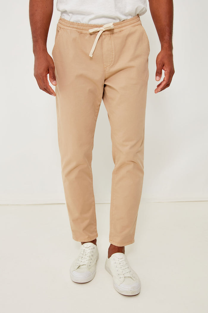 A person wears Marine Layer beige eco-friendly joggers, a white shirt, and white sneakers for a comfortable and stylish look.