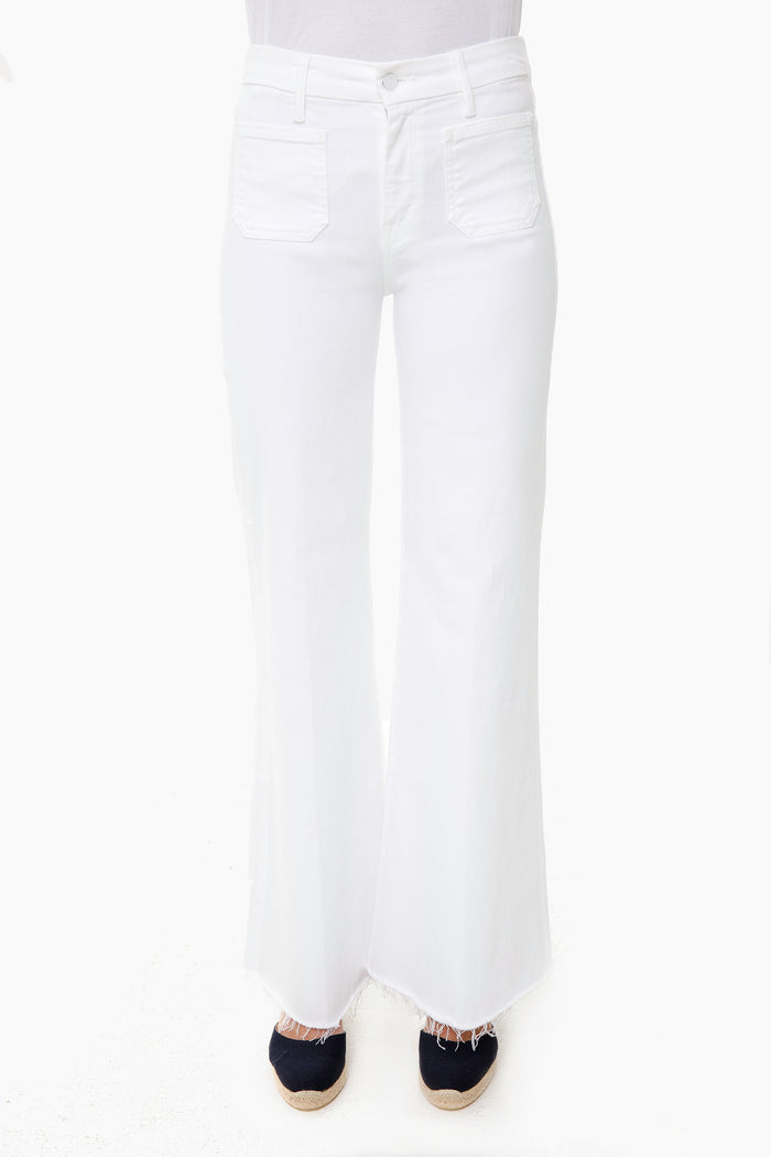 A person wears MOTHER high-rise, white wide-leg jeans with front pockets and frayed hems, paired with dark espadrille shoes.