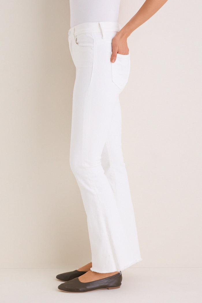 Person in classic slim-fit white jeans, Fairest Of Them All The Hustler Ankle Fray, with raw-edge hem, paired with black ballet flats; embodies effortless, high-end style.