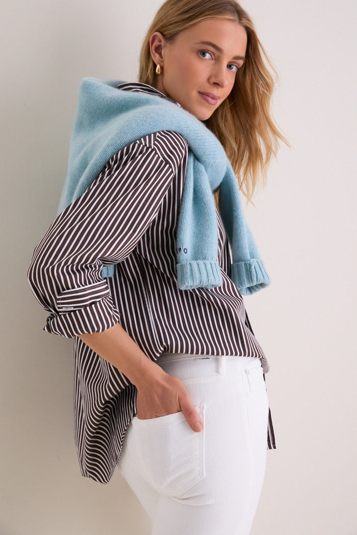 Young woman in a classic, effortlessly chic look wearing Fairest Of Them All The Hustler Ankle Fray jeans, styled with a striped shirt and light-blue sweater.