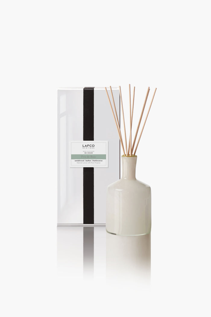 A white LAFCO New York diffuser bottle with reed sticks sits next to a matching white box with a black vertical stripe and the brand’s label, highlighting elegant home fragrances.