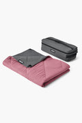A folded pink YETI Lowlands Blanket with a gray corner overlay is next to its gray YETI zippered carrying case, making it an ideal insulated outdoor picnic blanket.