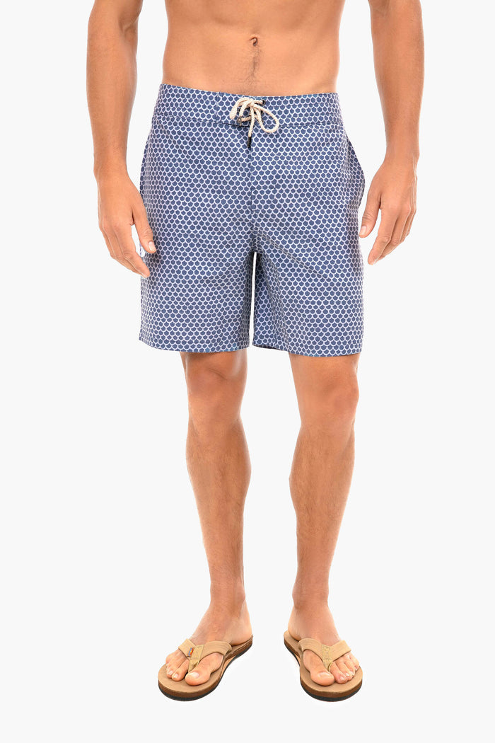 A man wears Faherty blue patterned board shorts with a drawstring and tan flip-flops, embracing surf culture.
