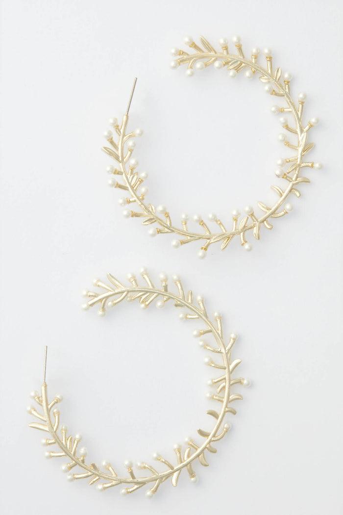 Nicola Bathie's large, circular gold hoop earrings are adorned with delicate pearls and leaf-shaped accents, creating a floral bud-inspired design.