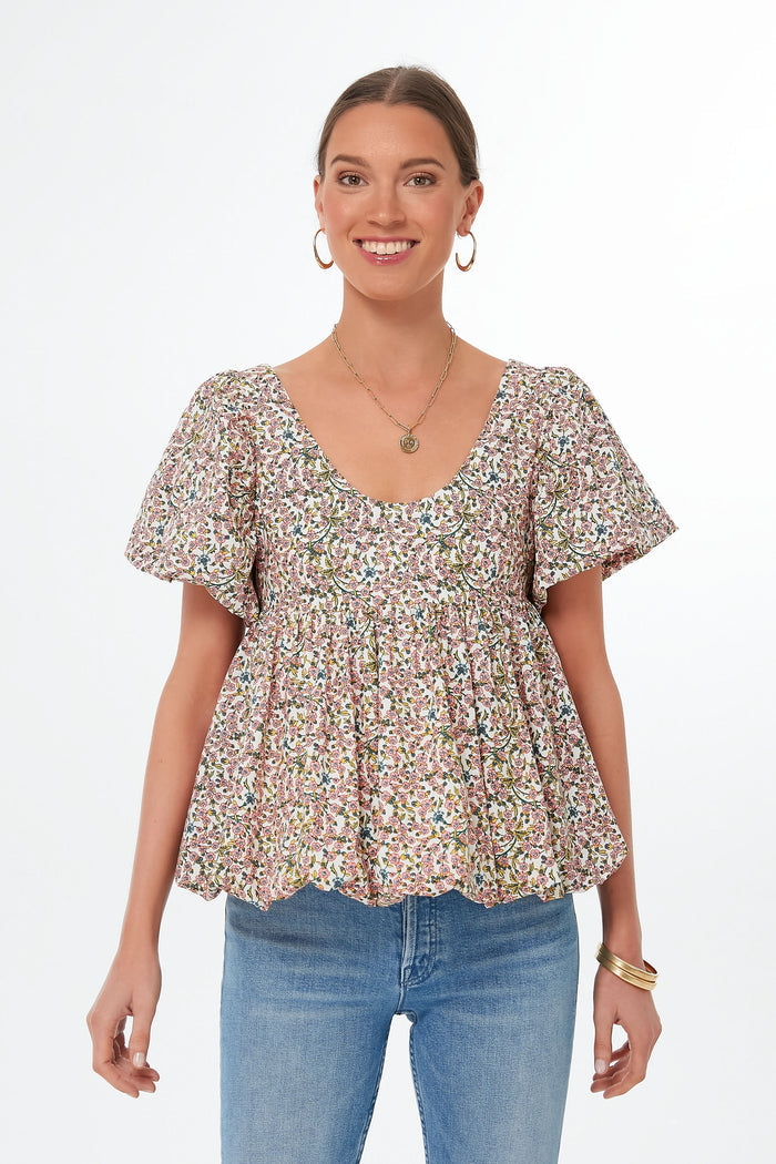 A woman stands smiling in a Hyacinth House floral puff-sleeve blouse and blue jeans.