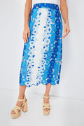 A person stands confidently in a blue and white Farm Rio floral midi skirt with a scalloped hem, paired with beige platform sandals.