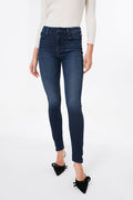 A person wears MOTHER dark blue mid-rise skinny jeans, a light long-sleeve top, and black pointed-toe shoes with bows.
