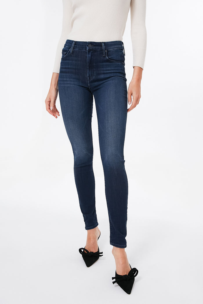 A person wears MOTHER dark blue mid-rise skinny jeans, a light long-sleeve top, and black pointed-toe shoes with bows.