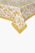 A Couleur Nature Paris handmade linen tablecloth features a yellow botanical floral and vine print bordering white fabric, elegantly draped over a table corner.