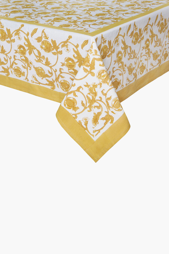 A Couleur Nature Paris handmade linen tablecloth features a yellow botanical floral and vine print bordering white fabric, elegantly draped over a table corner.
