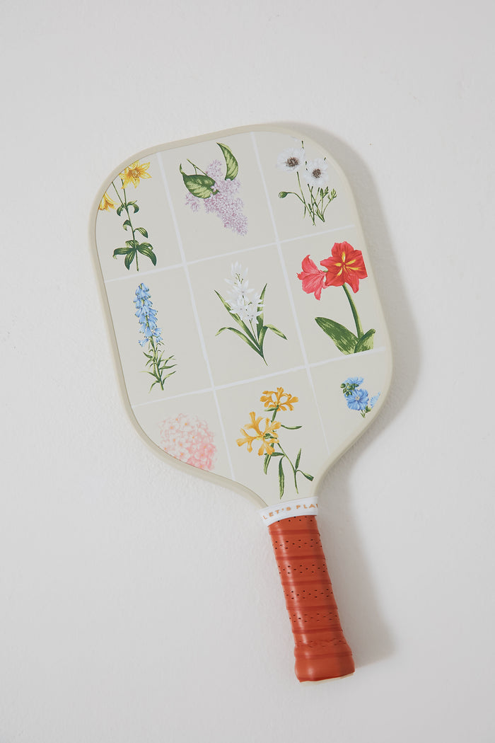 The Tnuck Sport x Recess Pickleball paddle features a red grip, a grid of colorful flowers on cream, and is made with fiberglass and a honeycomb core.