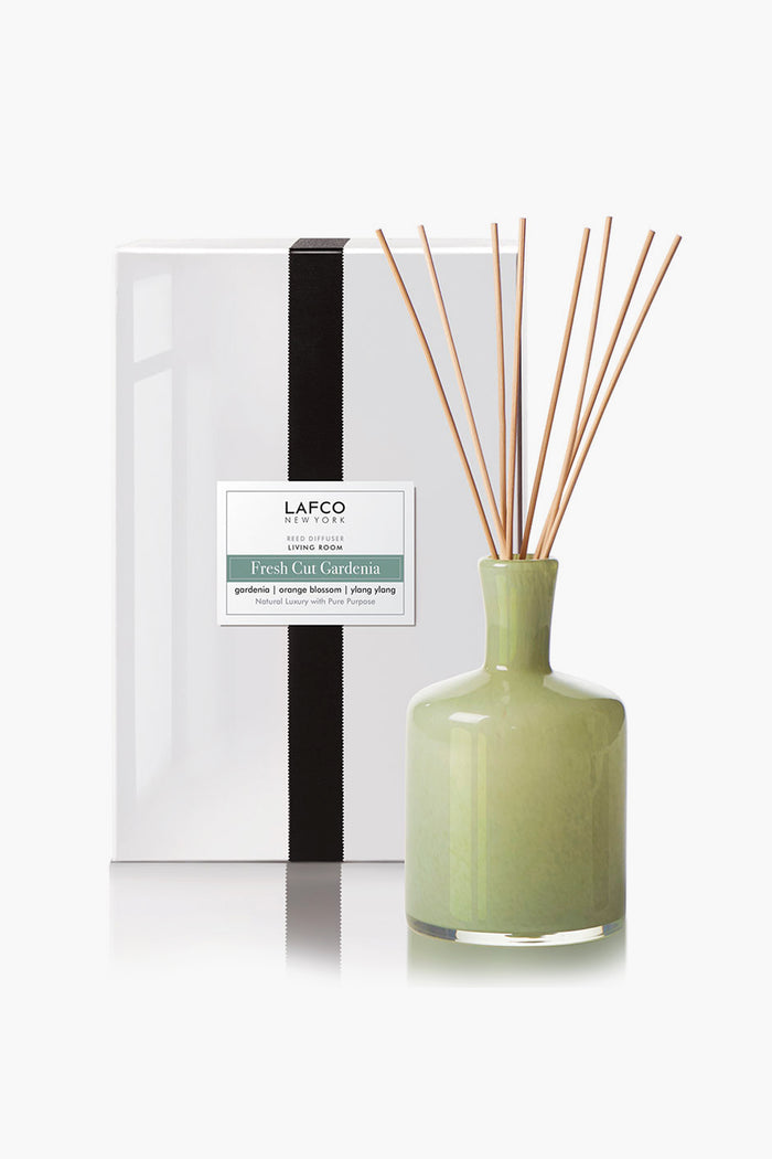 A green ceramic reed diffuser with sticks stands before a white LAFCO New York Fresh Cut Gardenia box, filling your space with elegant home fragrance and the fresh scent of gardenia.