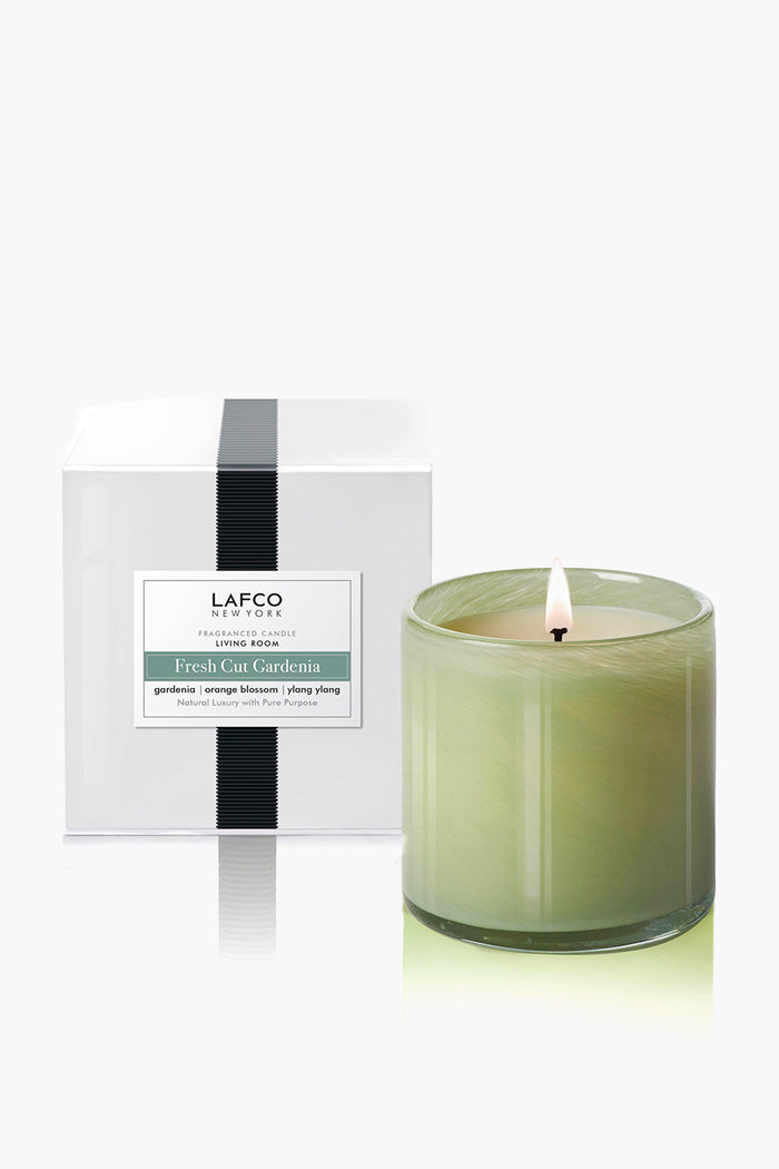 A lit LAFCO New York Fresh Cut Gardenia candle in hand-blown art glass sits before its white box packaging, ideal for enhancing your home fragrance.