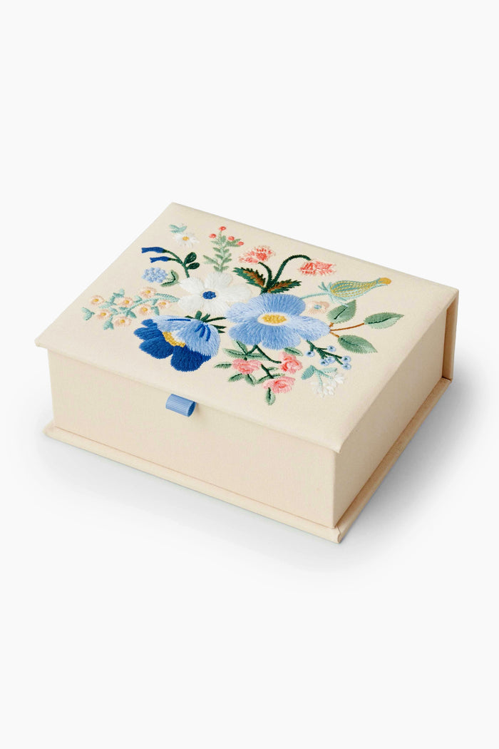 Rifle Paper Co.'s Garden Party Keepsake Box is a rectangular cream-colored fabric box, embroidered with blue, white, and pink flowers on the lid and finished with a blue ribbon pull.