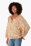 A woman wears the Love Tomas by Emerson Fry boho-chic floral button-up blouse with puffed long sleeves, paired with blue jeans.