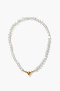 A Petit Moments white pearl necklace with gold-tone hardware and a heart-shaped magnetic closure, elegantly arranged in a circle.
