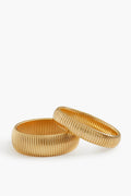 Two ribbed gold-plated brass bangles by Ben Amun are placed side by side, creating a striking statement jewelry piece.