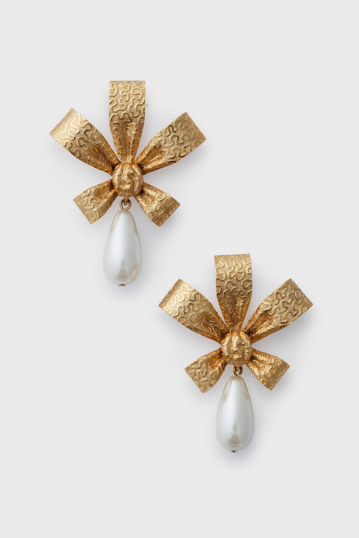 Handmade in New York, Jennifer Behr’s bow-shaped gold Holi earrings feature textured metal and dangling white teardrop pearls—a luxurious accessory.