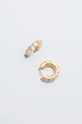 A pair of small Tuckernuck Jewelry Gold Huggie Hoop Earrings, one with clear gemstones and one plain, displayed on a white surface.
