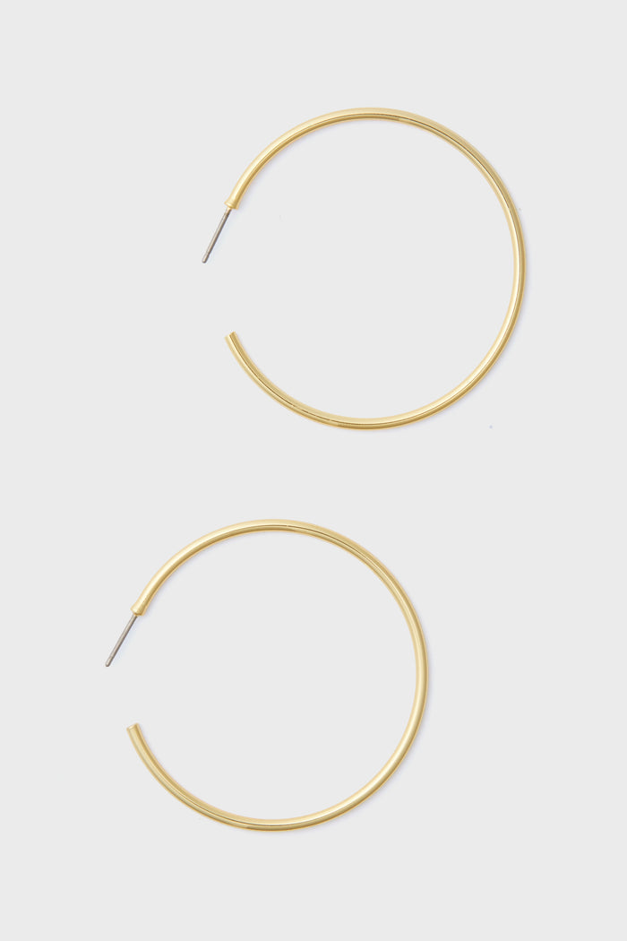 A pair of large, thin 14k gold plated hoop earrings with straight posts from Tuckernuck Jewelry—perfect hypoallergenic earrings for everyday style.