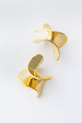 A pair of abstract, sculptural gold-plated Solana Earrings by Petit Moments featuring a wavy, folded design and an elegant swirl drop effect.