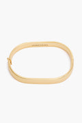 A vintage-inspired oval bangle from Jenny Bird, crafted from 14K gold-dipped brass with a smooth finish, hinged clasp, and "JENNY BIRD" engraved inside.