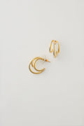 Two mismatched gold earrings from Alexa Leigh shine—one with overlapping crescent shapes, the other with two parallel 14k Gold Fill hoops—perfect for ear stacking or fans of our Triple Threat Earrings.