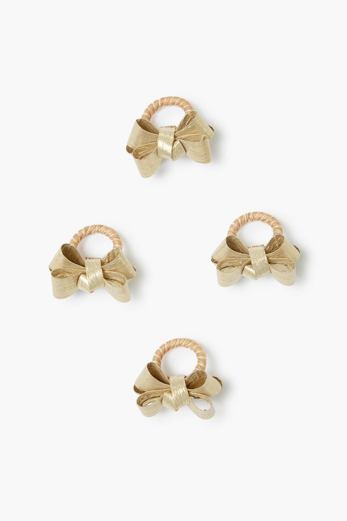 Juliska's four gold bow hair ties are elegantly arranged, each one resembling a chic table decor accent or a delicate gold napkin ring.