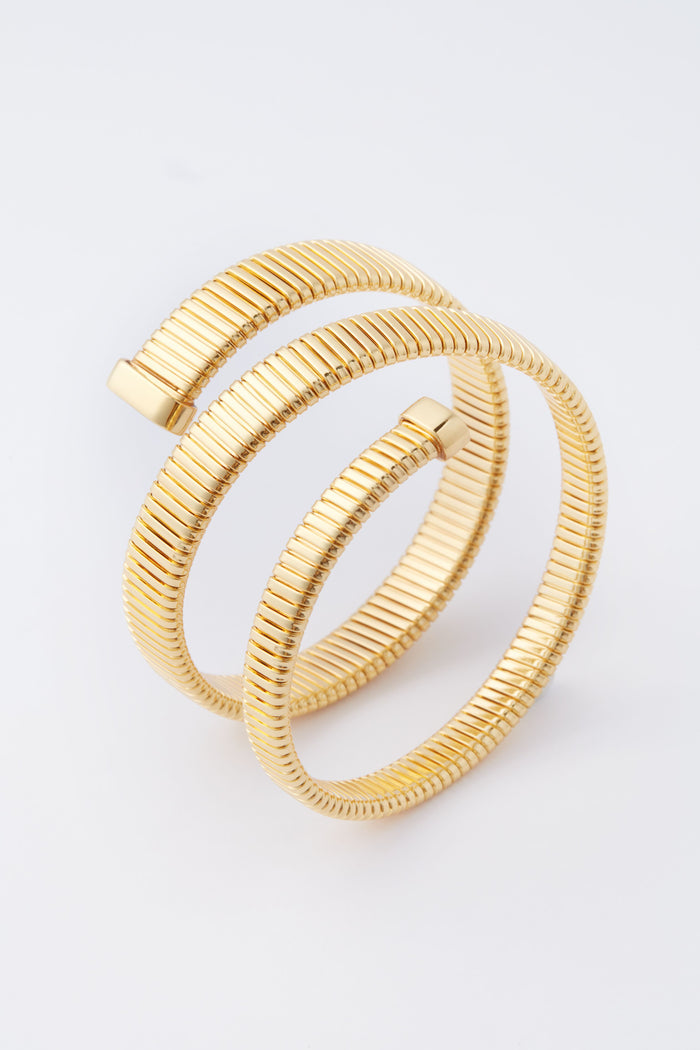 A gold-plated, coiled serpent chain bracelet with ribbed texture and two open ends by Tuckernuck Jewelry—a stunning statement piece.