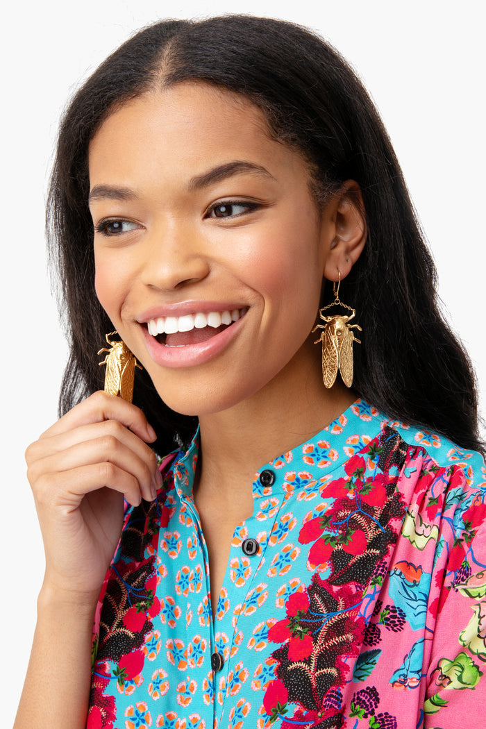 Young woman wearing classic, oversized Goldbug Large Drop Earrings with a cicada design, embodying a fun and high-end Charleston-inspired style, effortlessly complementing her floral-print shirt.