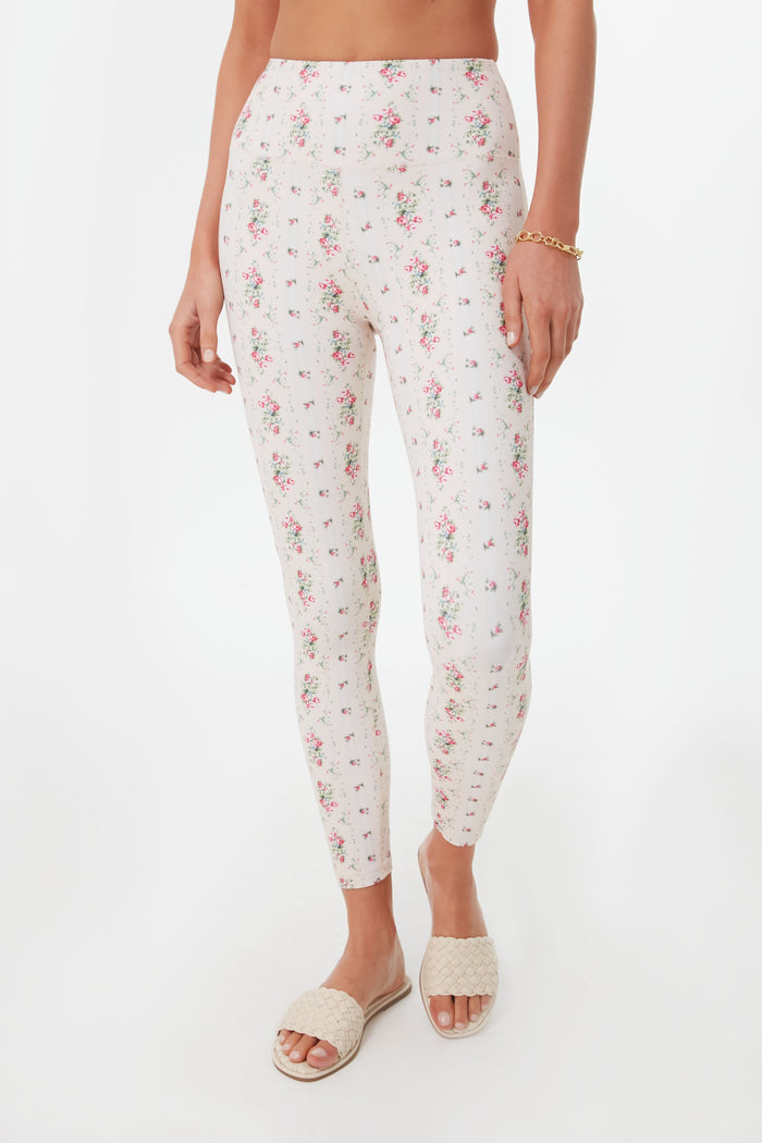 A person wears LoveShackFancy high-waisted floral print leggings with a smocked waistband, beige woven slide sandals, and a gold bracelet.