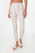 A person wears LoveShackFancy high-waisted floral print leggings with a smocked waistband, beige woven slide sandals, and a gold bracelet.