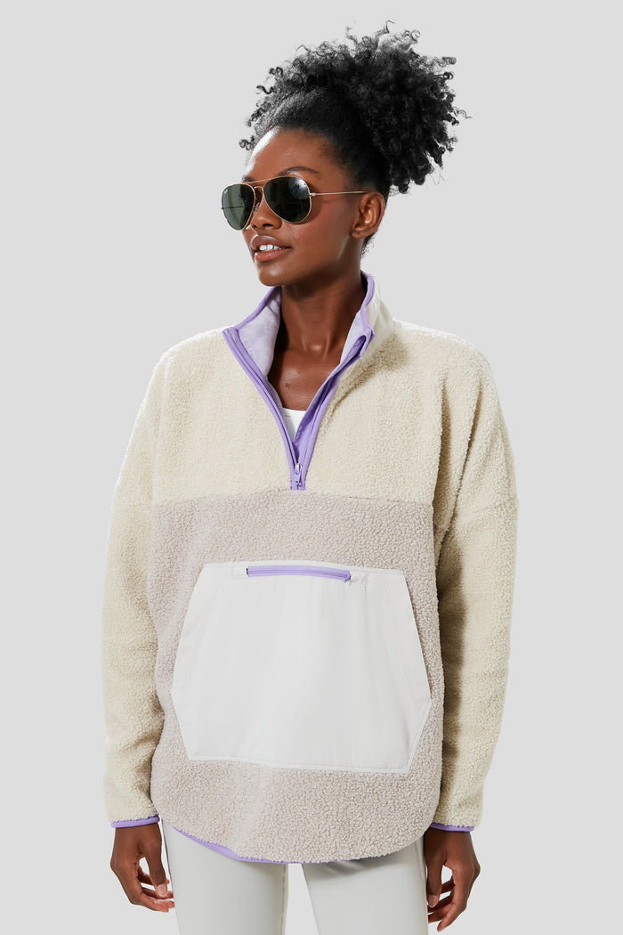 A person in sunglasses and a Tnuck Sport Gray and Lilac Fleece Cady quarter zip pullover with front pocket stands confidently, highlighting cozy style.