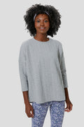 A woman models Tnuck Sport’s relaxed-fit light gray quilted long-sleeve top paired with blue patterned leggings.