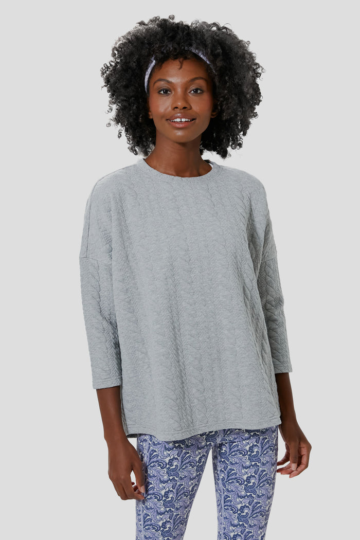 A woman models Tnuck Sport’s relaxed-fit light gray quilted long-sleeve top paired with blue patterned leggings.