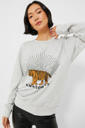 A woman wears an Emerson Fry light gray French terry Tiger Sweatshirt with radiating lines, paired with black pants and posing with one hand behind her head. Made in the USA.