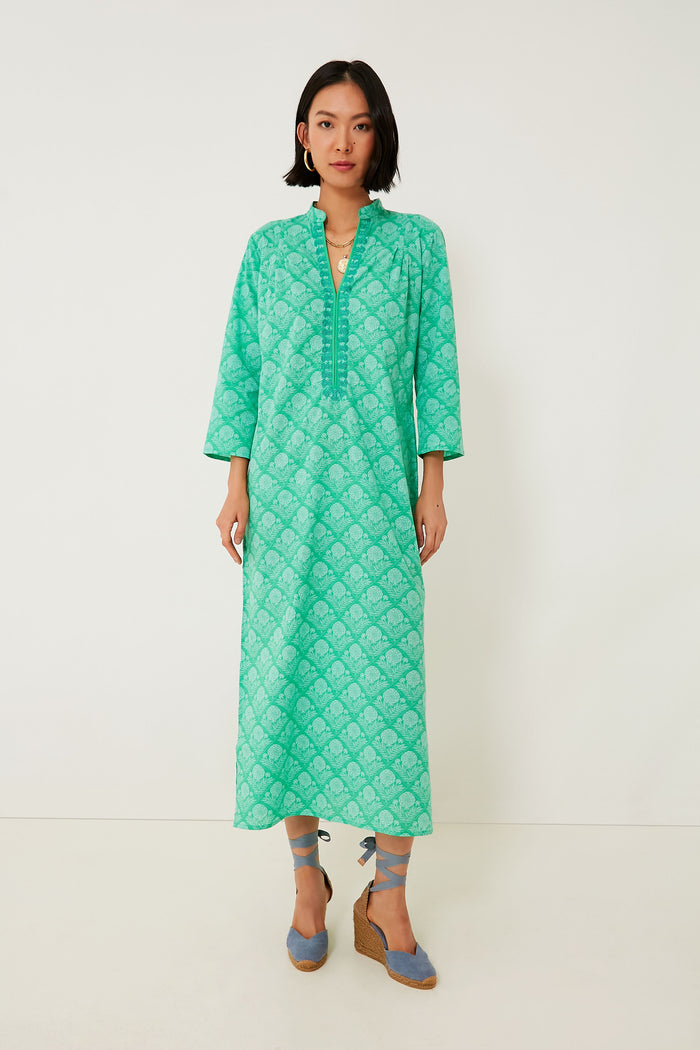 A woman models a Ro's Garden long, green patterned caftan dress with three-quarter sleeves and blue wedge sandals, capturing a boho-chic vibe ideal for luxury travel.