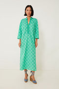 A woman models a Ro's Garden long, green patterned caftan dress with three-quarter sleeves and blue wedge sandals, capturing a boho-chic vibe ideal for luxury travel.