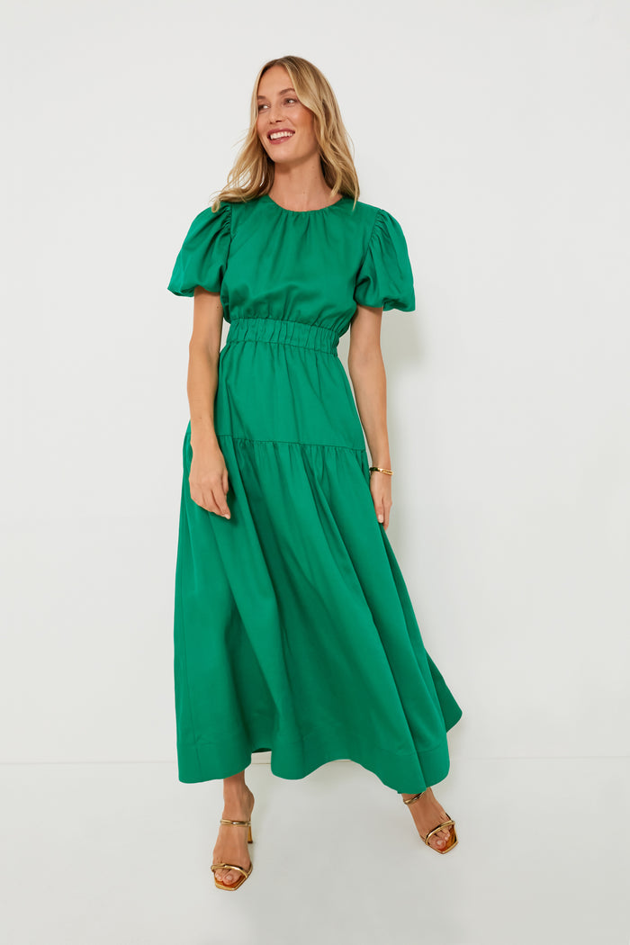 A woman in a green bohemian maxi dress from Hyacinth House, wearing gold sandals, with loose blonde hair and a relaxed smile.