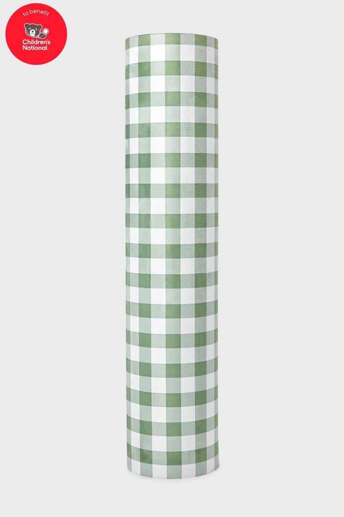 A roll of green and white checkered paper stands upright. A red circle in the top left features the Children’s National Hospital logo, echoing the lively design of the Tuckernuck x Jollie Green Trellis Yoga Mat.