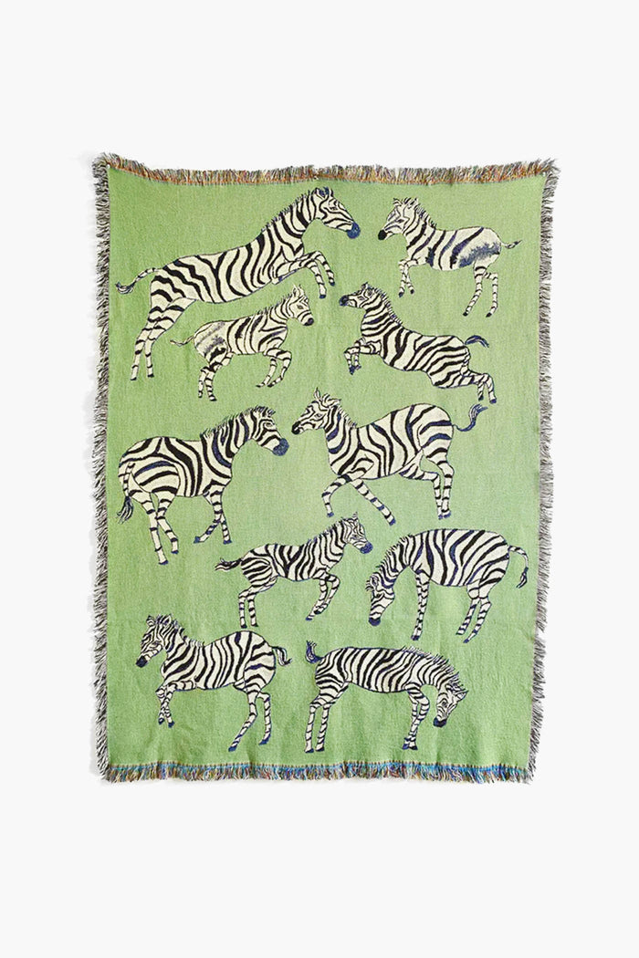 The Olivia Wendel Green Zebras Blanket is a lightweight throw made from 100% US-grown cotton, featuring playful black and white zebras in various poses on a green background.