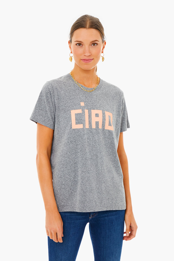 A woman wears a gray Clare V tee with pink "CIAO" lettering, paired with blue jeans and gold accessories, creating an effortlessly chic, Parisian-inspired look.