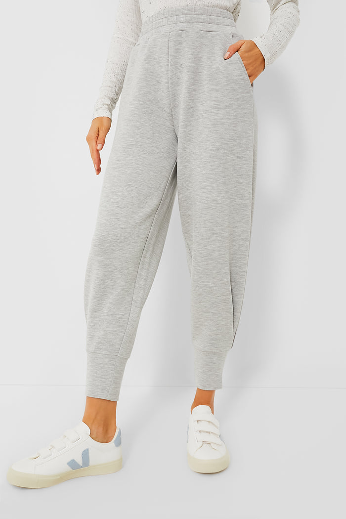 A person wears Varley Grey Marl Relaxed Pant, a long-sleeve white textured top, and white sneakers with pale blue accents, exemplifying performance-fashion style.
