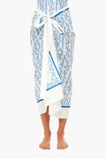 A person stands barefoot wearing an AGUA BY AGUA BENDITA white and blue patterned cotton-silk sarong tied at the waist.