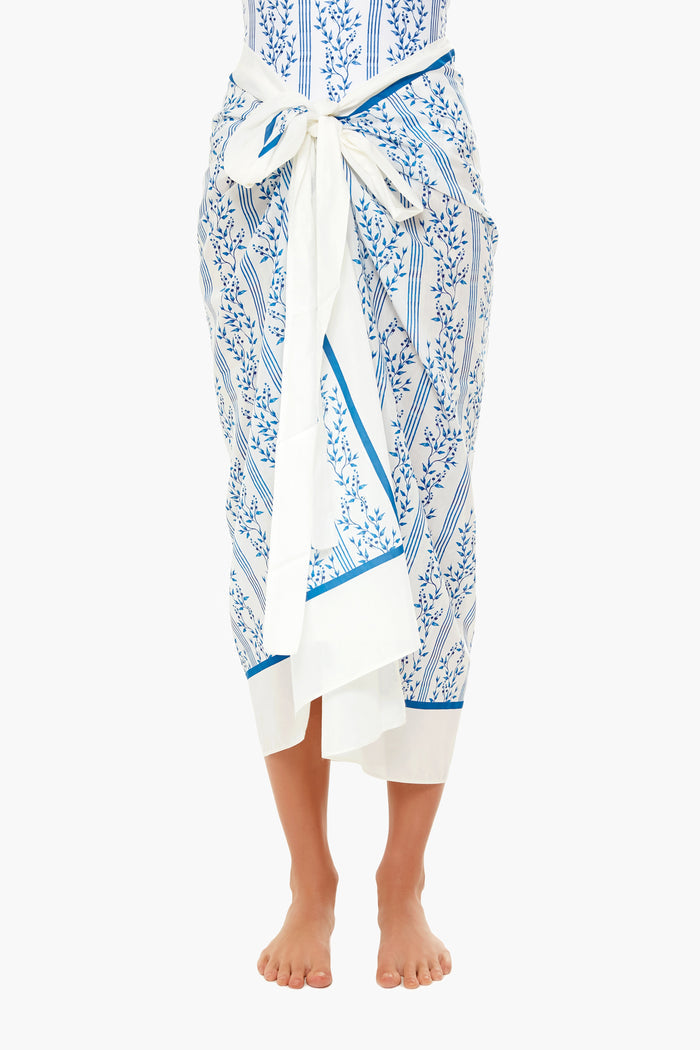 A person stands barefoot wearing an AGUA BY AGUA BENDITA white and blue patterned cotton-silk sarong tied at the waist.