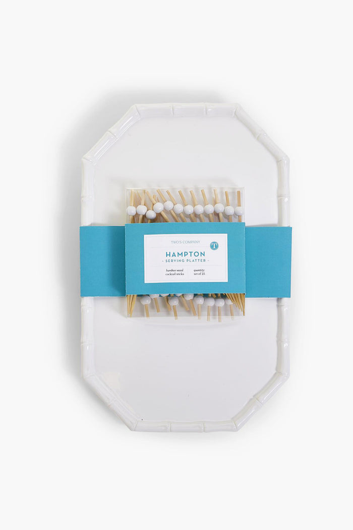 This Two's Company set includes a white chinoiserie serving platter with a faux bamboo-style rim, packaged in a blue paper band and paired with wooden cocktail picks featuring decorative white and blue tops.