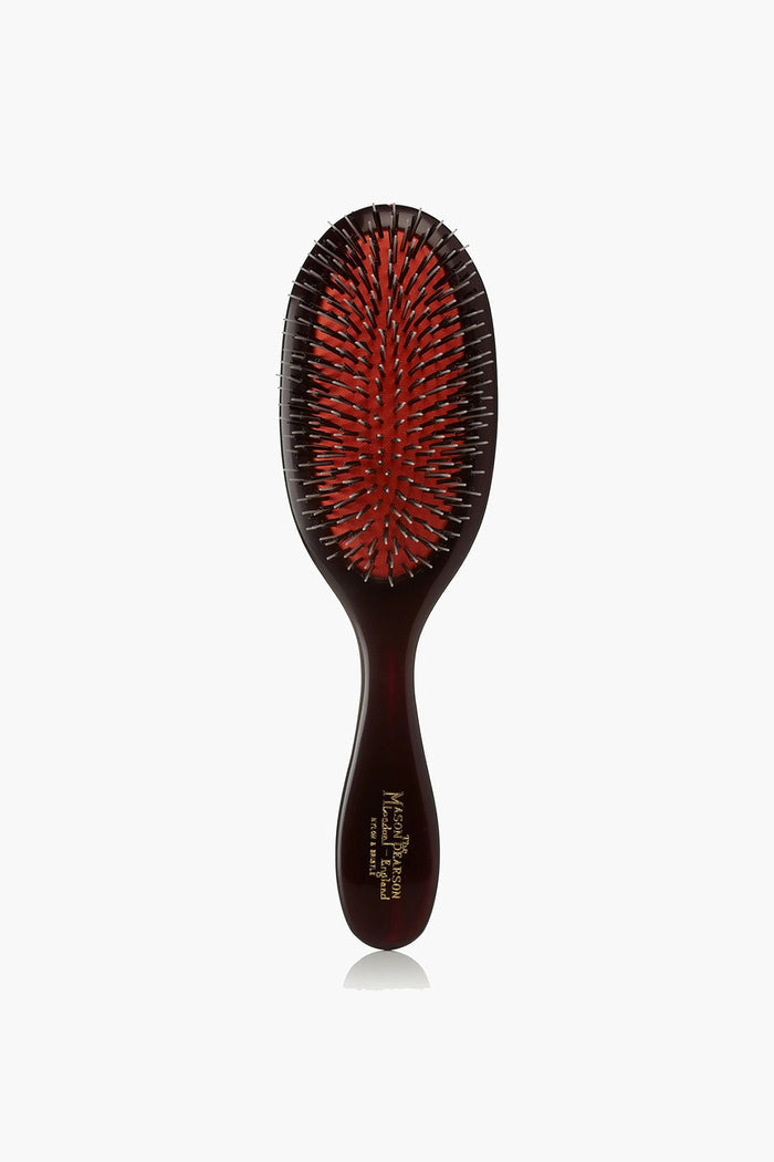 A Mason Pearson hair grooming tool featuring a dark handle, a red cushion, and a mix of black and silver bristles.