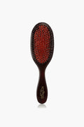 A Mason Pearson hair grooming tool featuring a dark handle, a red cushion, and a mix of black and silver bristles.