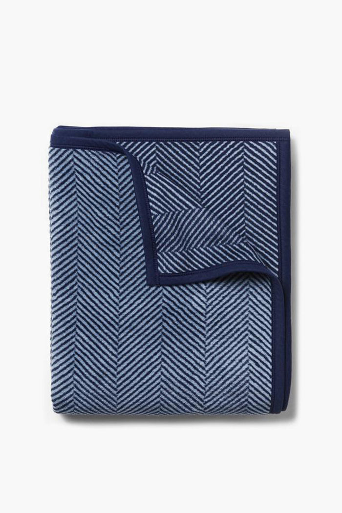 A machine-washable ChappyWrap blanket, neatly folded in a blue and navy herringbone pattern with a solid navy border.