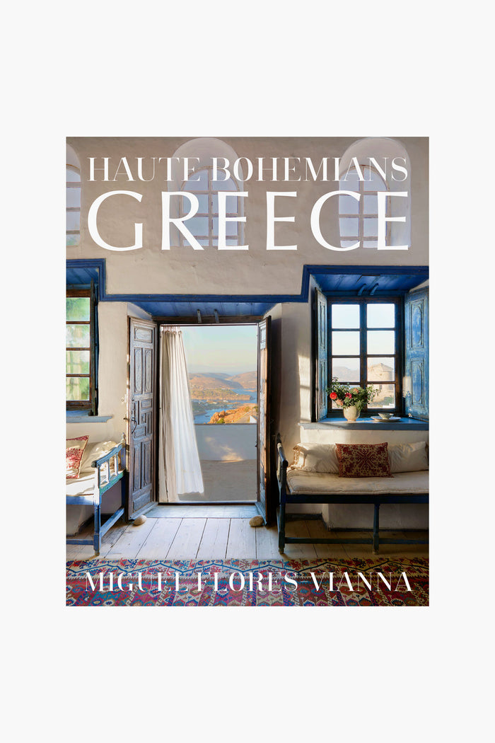The cover of Haute Bohemians Greece by Miguel Flores-Vianna, published by Abrams Books, features a Greek-style interior with open doors, sea view, blue windows, and rustic furniture that highlight the charm of Greek architecture.